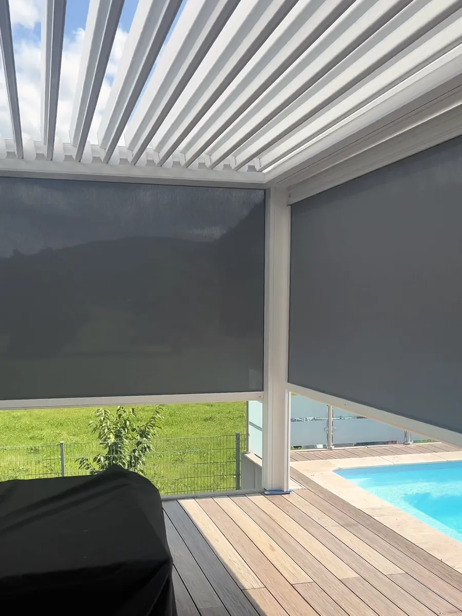 Weißes Lamellendach mit geöffneten Lamellen, zwei Senkrechtmarkisen halb unten, daneben der Pool