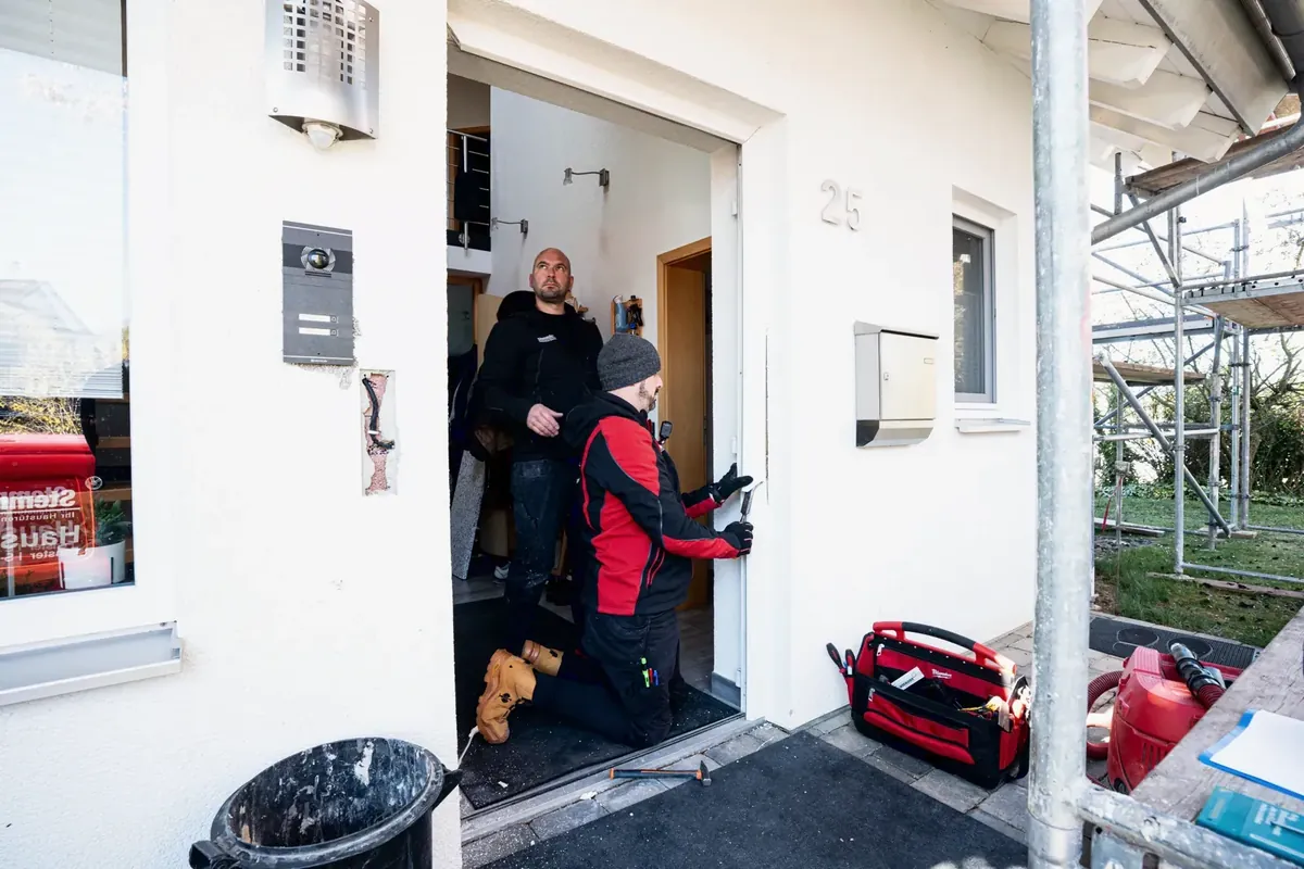 Zwei Monteure bei der Arbeit an einem Hauseingang mit Gerüst