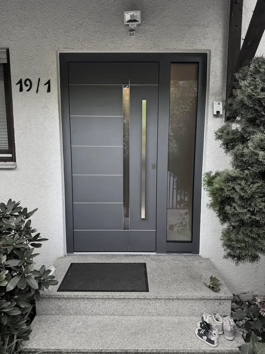 Anthrazitfarbene Haustür mit Edelstahl-Rillen und Glas-Seitenteil