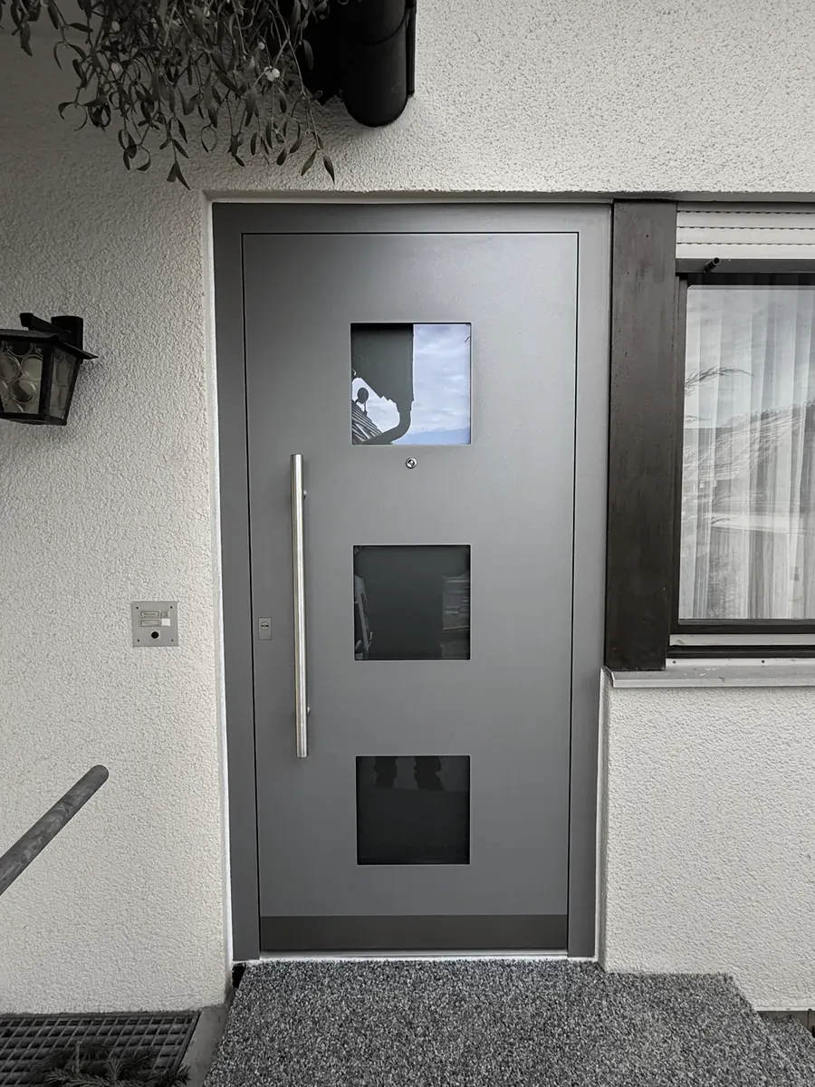 Graue Haustür mit drei quadratischen Glasausschnitten